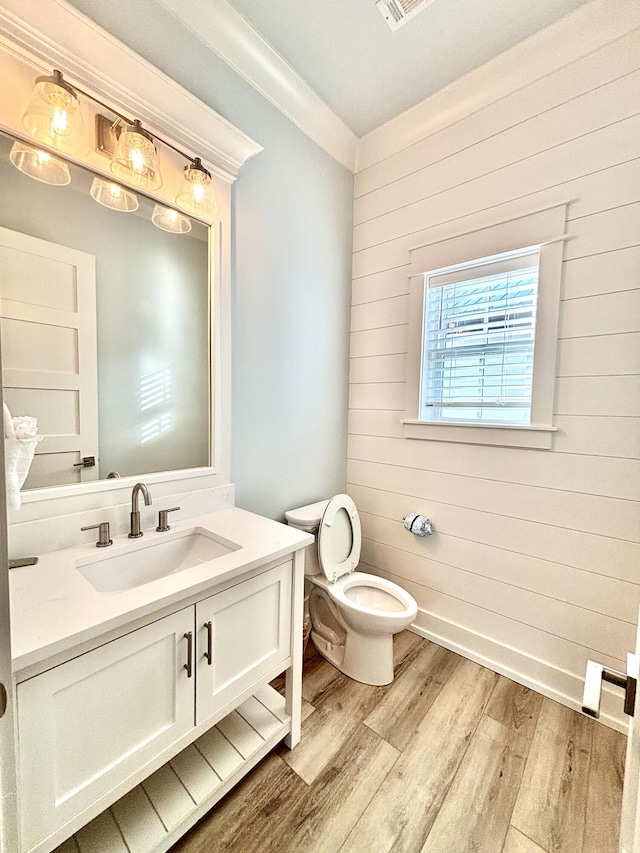 bathroom with hardwood / wood-style floors, vanity, wood walls, crown molding, and toilet