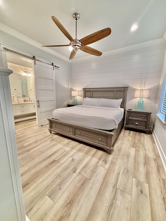 bedroom featuring ensuite bath, ornamental molding, ceiling fan, a barn door, and light hardwood / wood-style flooring