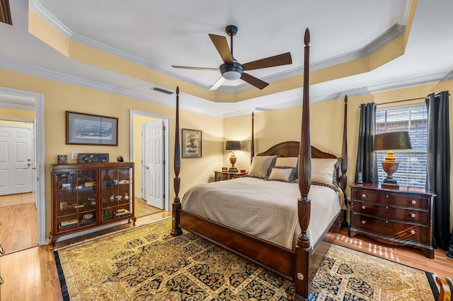 bedroom with hardwood / wood-style floors, ceiling fan, a raised ceiling, and ornamental molding