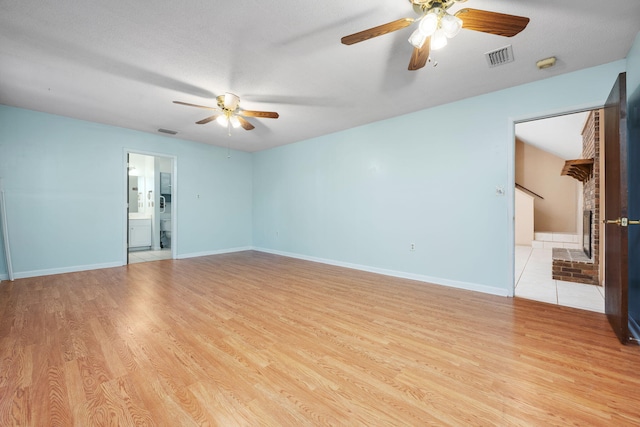 spare room with ceiling fan, light hardwood / wood-style floors, a textured ceiling, and a brick fireplace