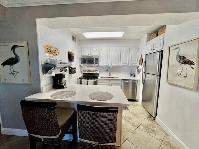 kitchen with sink, kitchen peninsula, appliances with stainless steel finishes, tasteful backsplash, and white cabinetry