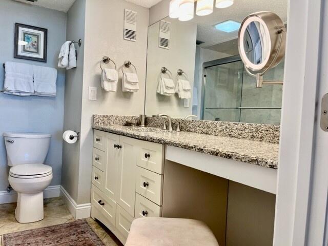 bathroom featuring tile patterned flooring, vanity, toilet, and a shower with shower door