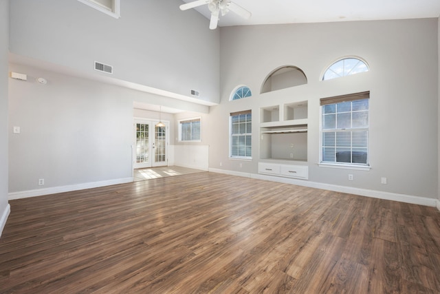 unfurnished living room with ceiling fan, dark hardwood / wood-style flooring, a towering ceiling, and a wealth of natural light