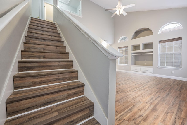 stairway featuring hardwood / wood-style flooring, ceiling fan, a towering ceiling, and built in shelves