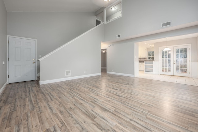 unfurnished living room featuring light hardwood / wood-style flooring, high vaulted ceiling, and french doors