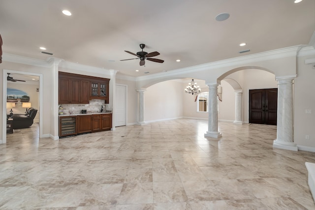 unfurnished living room with decorative columns, wine cooler, ceiling fan with notable chandelier, and ornamental molding