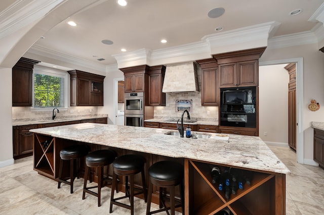 kitchen featuring ornamental molding, premium range hood, light stone counters, and a large island