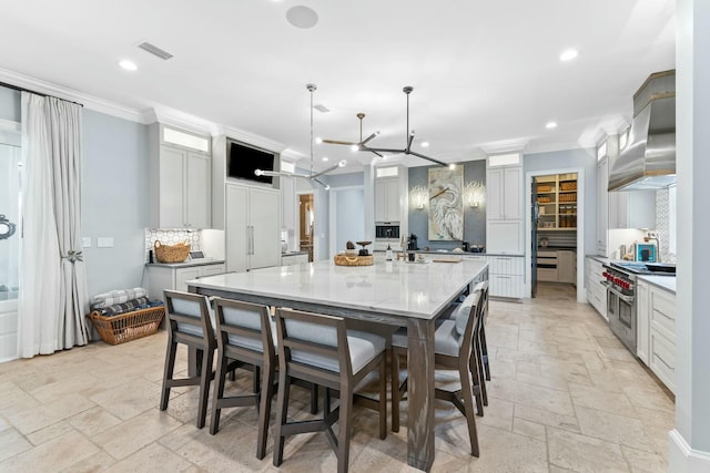 kitchen featuring wall chimney range hood, light stone counters, pendant lighting, a spacious island, and range with two ovens