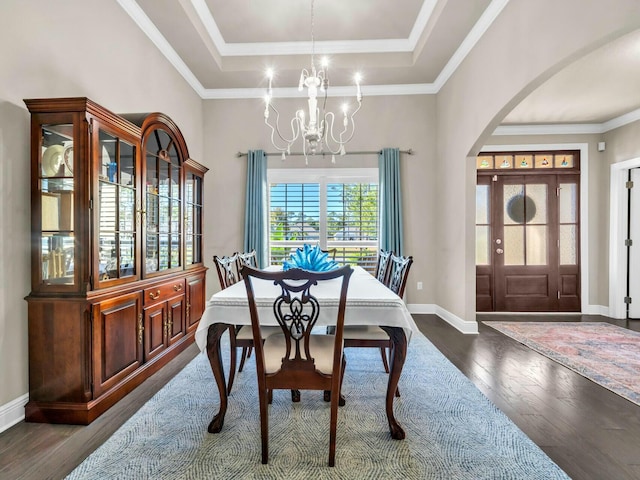 dining area featuring a notable chandelier, dark wood-type flooring, ornamental molding, and a raised ceiling