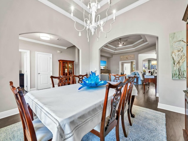 dining area featuring ornamental molding, dark wood-type flooring, a raised ceiling, and ceiling fan with notable chandelier