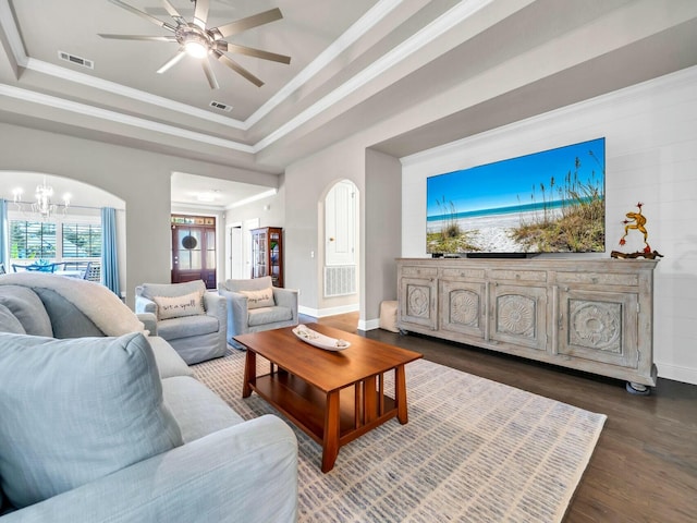 living room with ornamental molding, dark wood-type flooring, ceiling fan with notable chandelier, and a tray ceiling