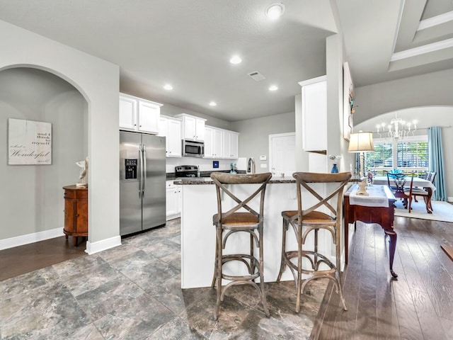 kitchen featuring kitchen peninsula, a notable chandelier, white cabinetry, dark stone counters, and appliances with stainless steel finishes