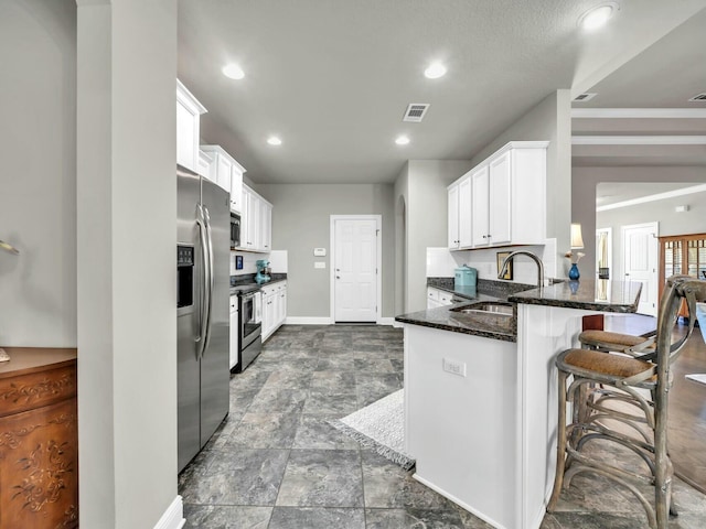 kitchen with kitchen peninsula, stainless steel appliances, white cabinets, dark stone countertops, and sink