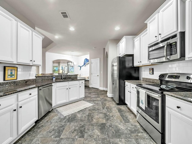 kitchen with an inviting chandelier, white cabinetry, appliances with stainless steel finishes, dark stone countertops, and sink