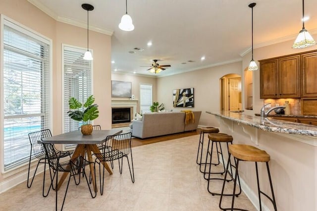 kitchen featuring brown cabinets, ornamental molding, light stone counters, arched walkways, and a fireplace