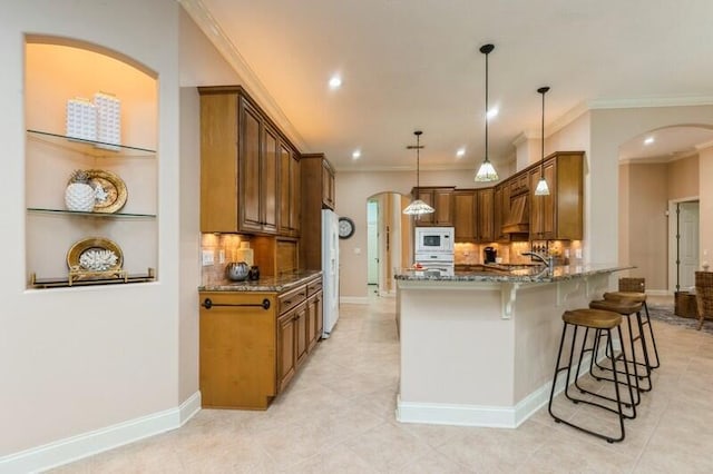 kitchen with a kitchen bar, dark stone countertops, white appliances, arched walkways, and a peninsula