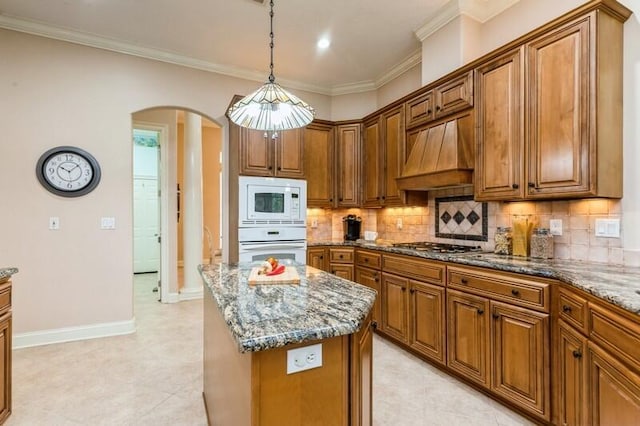 kitchen with brown cabinetry, white appliances, custom exhaust hood, and arched walkways