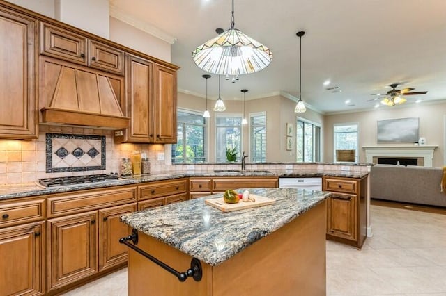 kitchen with stainless steel gas cooktop, a sink, wall chimney exhaust hood, brown cabinets, and a center island