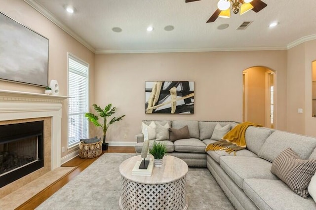 living room featuring visible vents, baseboards, a fireplace with flush hearth, ornamental molding, and wood finished floors