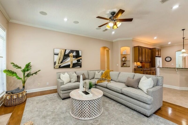 living room with ornamental molding, baseboards, arched walkways, and light wood-type flooring