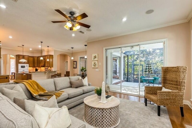 living room featuring visible vents, arched walkways, light wood-style flooring, and ornamental molding