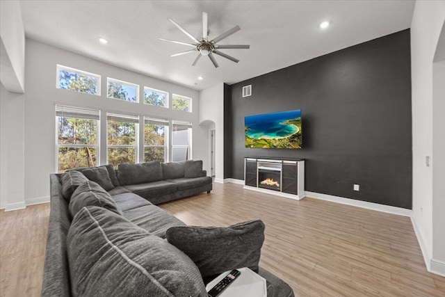 living room with ceiling fan, light hardwood / wood-style flooring, and a high ceiling