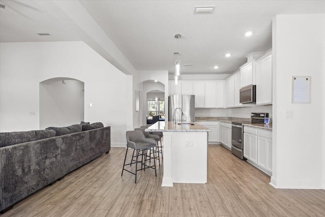 kitchen with white cabinetry, an island with sink, stainless steel appliances, and light wood-type flooring