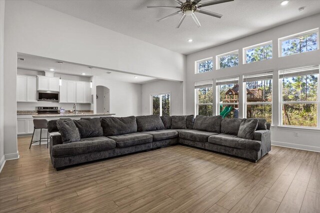 living room with a textured ceiling, a towering ceiling, light hardwood / wood-style flooring, and ceiling fan