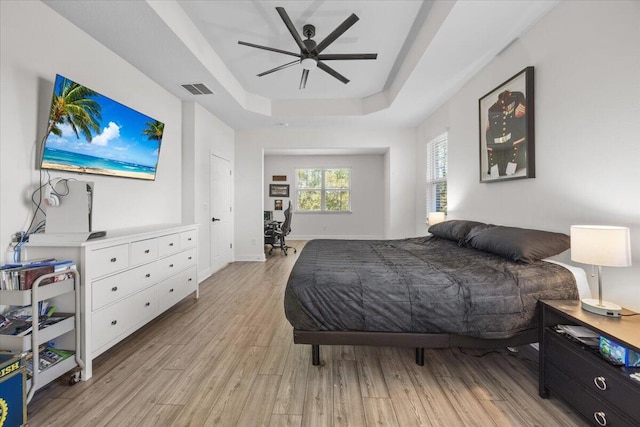 bedroom with a tray ceiling, ceiling fan, and light wood-type flooring