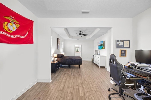 bedroom featuring a tray ceiling, light hardwood / wood-style floors, and a textured ceiling