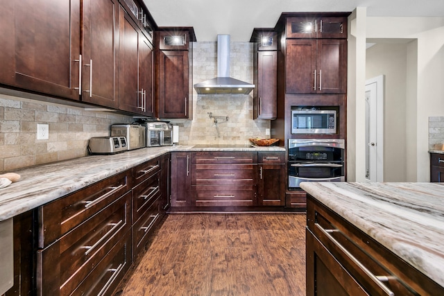 kitchen with dark wood-type flooring, wall chimney range hood, tasteful backsplash, light stone counters, and stainless steel appliances