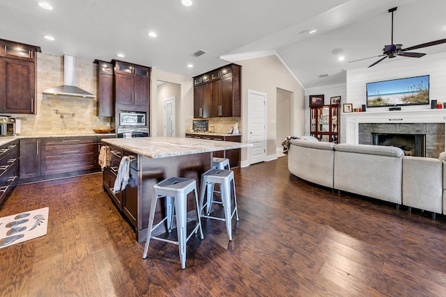 kitchen with backsplash, lofted ceiling, a kitchen island, and wall chimney range hood