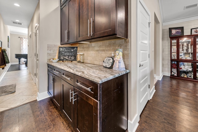 kitchen featuring dark hardwood / wood-style floors, decorative backsplash, light stone countertops, ornamental molding, and dark brown cabinets