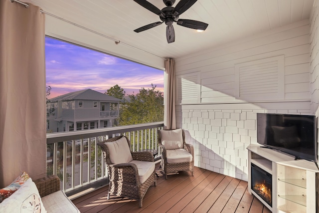 deck at dusk featuring ceiling fan and an outdoor fireplace