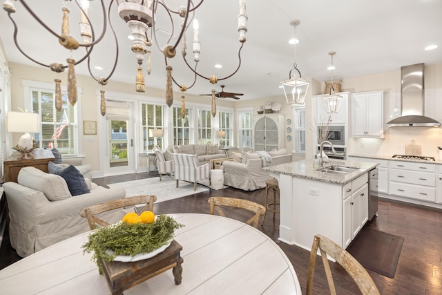 kitchen featuring a center island with sink, stainless steel appliances, decorative backsplash, wall chimney range hood, and light stone counters