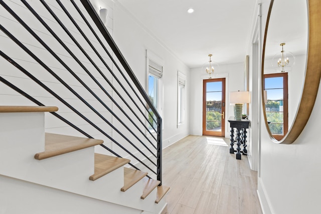 foyer entrance with ornamental molding, light wood-type flooring, and an inviting chandelier