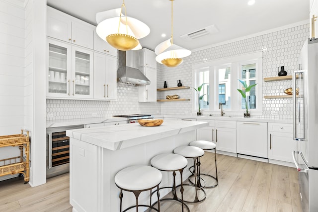 kitchen with refrigerator, white dishwasher, wall chimney range hood, white cabinets, and a center island