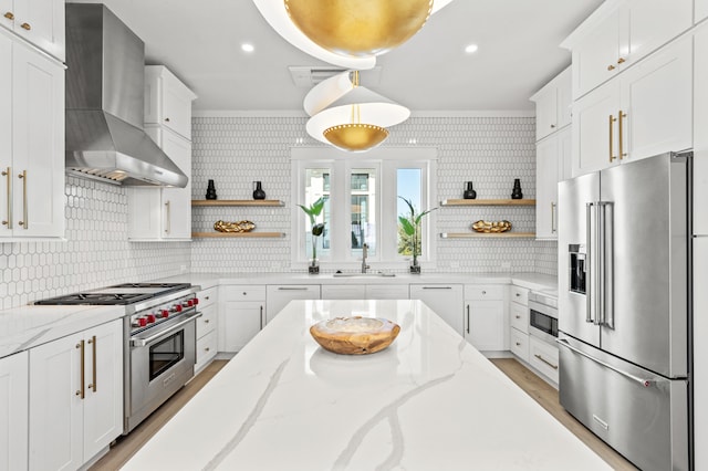 kitchen featuring light stone countertops, ornamental molding, premium appliances, wall chimney range hood, and white cabinetry