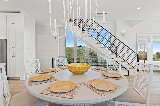 dining space with light wood-type flooring, wooden walls, and a notable chandelier