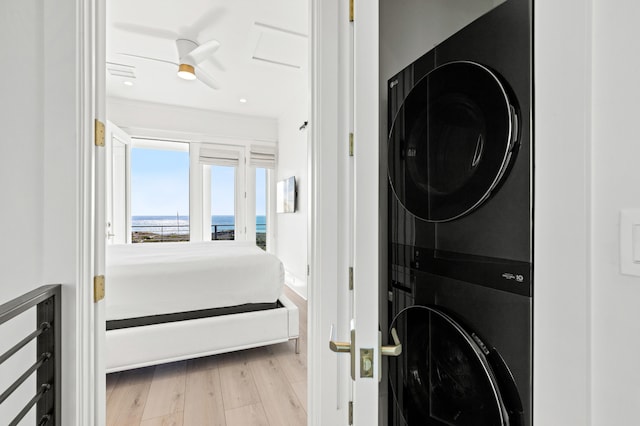 laundry room with light wood-type flooring, stacked washer and dryer, ceiling fan, and a water view