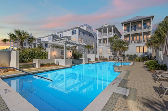 pool at dusk featuring a pergola and a patio