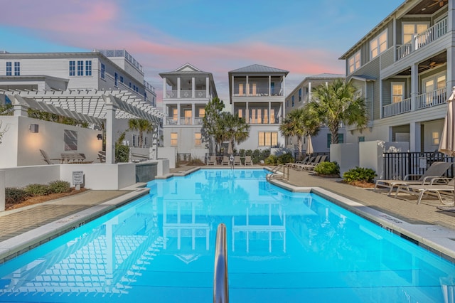 pool at dusk featuring a pergola