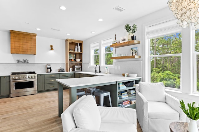 kitchen with gray cabinetry, high end stainless steel range oven, sink, an inviting chandelier, and light hardwood / wood-style floors