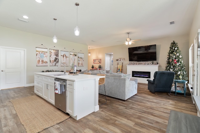 kitchen featuring stainless steel dishwasher, sink, white cabinetry, hanging light fixtures, and an island with sink