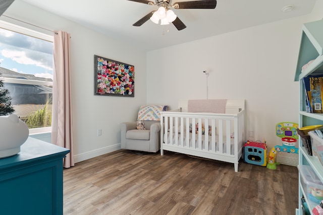 bedroom with hardwood / wood-style flooring, a nursery area, and ceiling fan