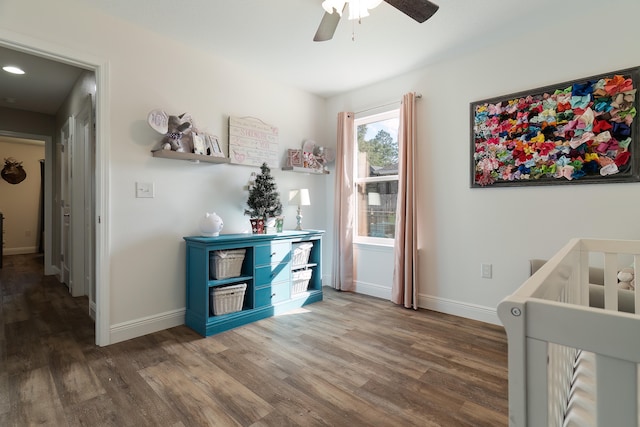 bedroom with ceiling fan, dark wood-type flooring, and a nursery area