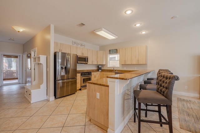 kitchen featuring a breakfast bar area, light brown cabinetry, light stone counters, kitchen peninsula, and stainless steel appliances