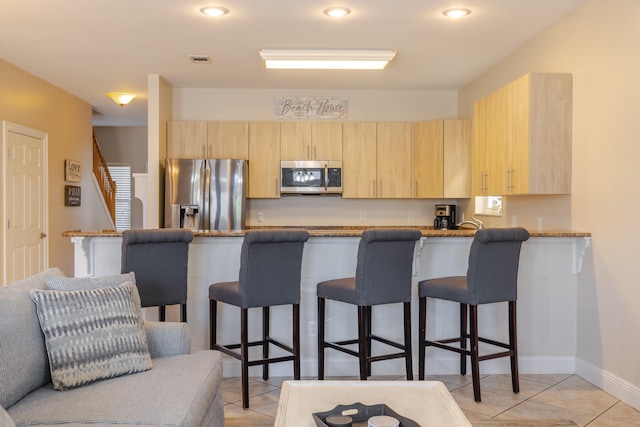 kitchen with a kitchen breakfast bar, light brown cabinets, kitchen peninsula, and appliances with stainless steel finishes