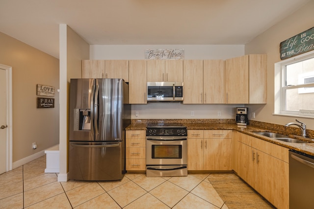 kitchen featuring sink, stainless steel appliances, dark stone counters, light brown cabinetry, and light tile patterned floors