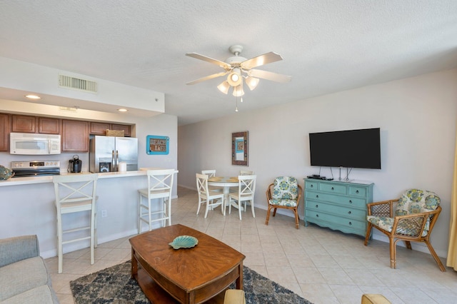 living room featuring ceiling fan, light tile patterned floors, and a textured ceiling